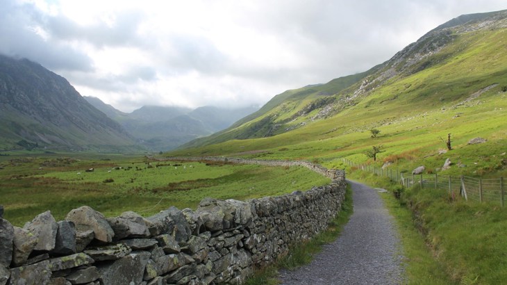 A gravel path winding its way into the green hills alongside a stone wall.