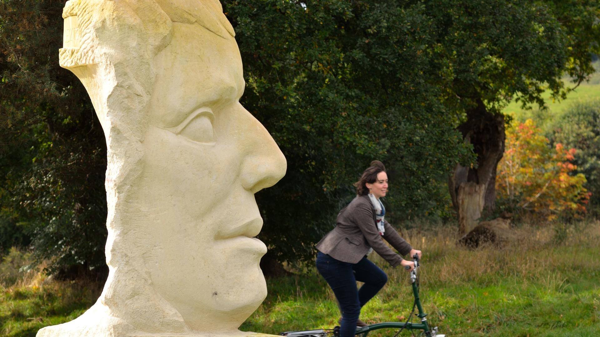 Woman cycling past a large sculpture of The Father of the Bicycle Industry