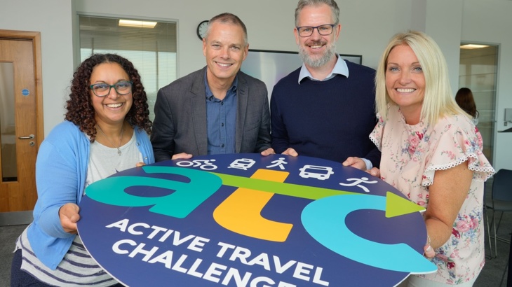 Two smiling women and two smiling men hold a large circular disc in front of them with the wording 'atc active travel challenge' on it.
