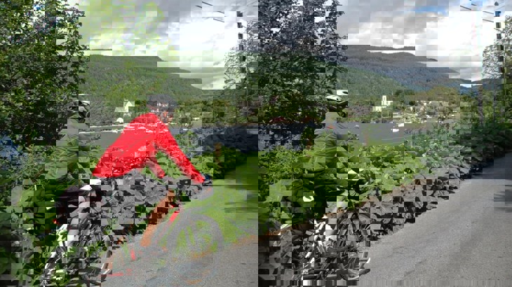 Cycle tourer on a road beside river and mountains