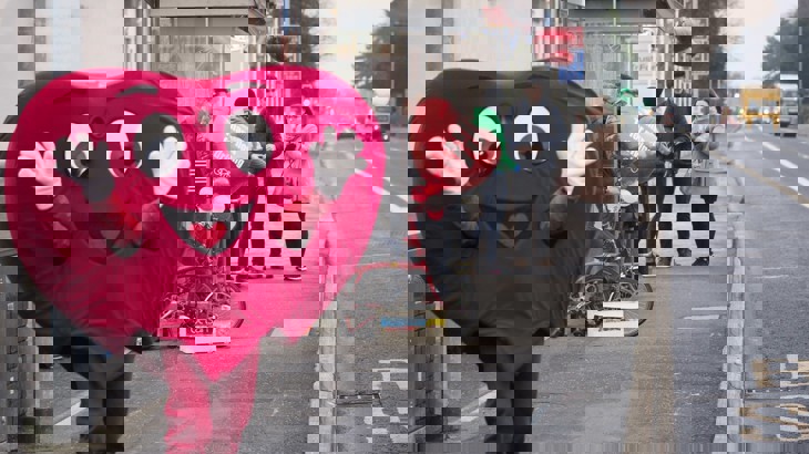 Walk Wheel Cycle Trust heart-shaped air quality mascot stands at a bus stop. 