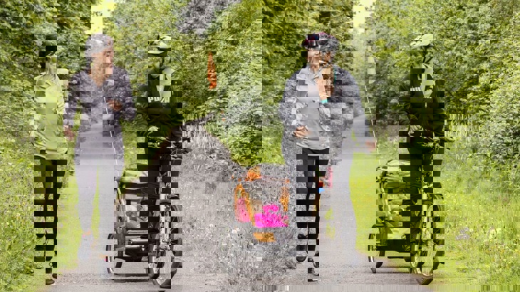 A runner and a cyclist pulling a pink trailer with child in it on traffic-free greenway