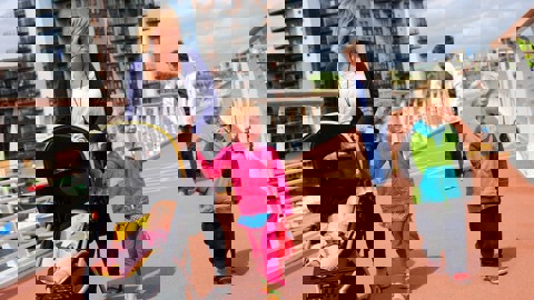 Woman with baby in pushchair with two small children and older woman, walking over bridge in urban area