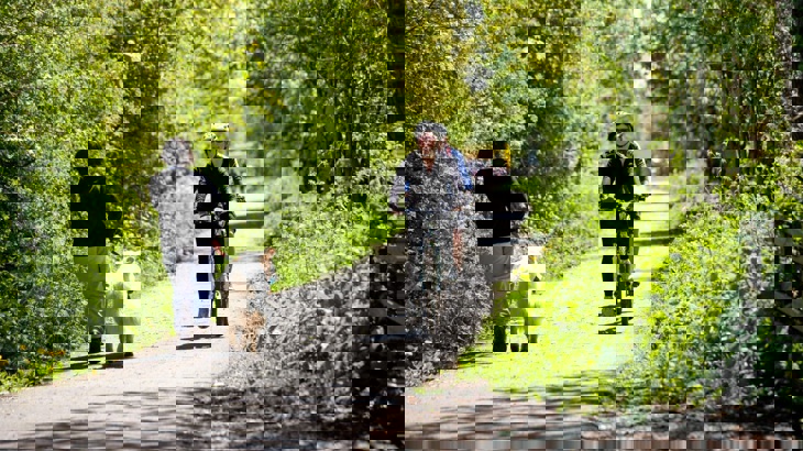 Cyclists and dog walker with white dog on tarmac cycle path with green verges