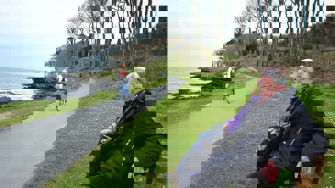 Couple sitting on park bench, looking at cyclist on coastal cycle path