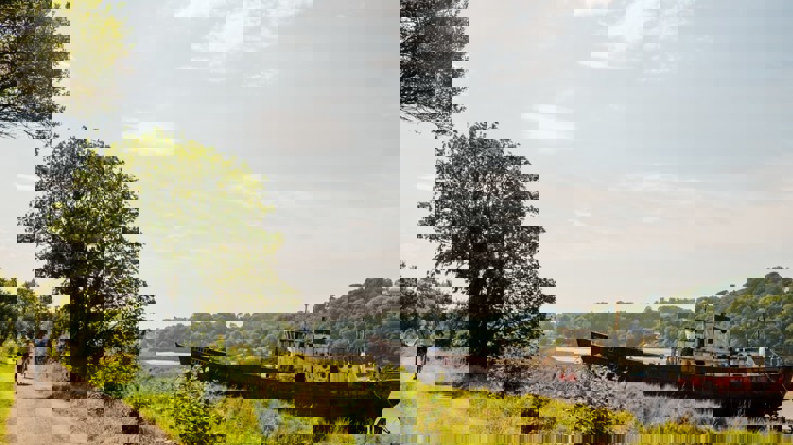 Cyclists on cycle path going past abandoned boat in estuary