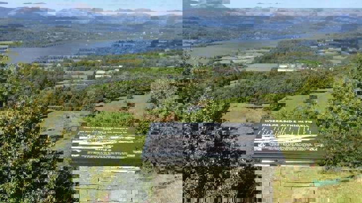 View of Lake Windermere with hills and trees in background and interpretation board in the foreground