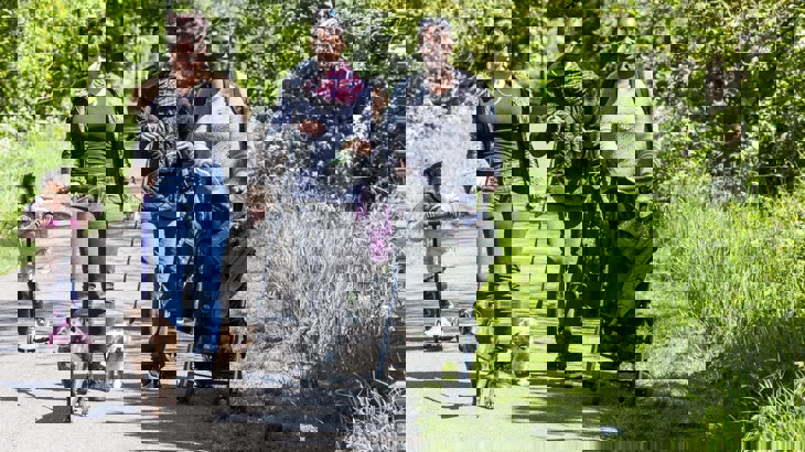 Little girl on scooter, two women walking dogs, one woman with pushchair and boy behind the group on cycle path