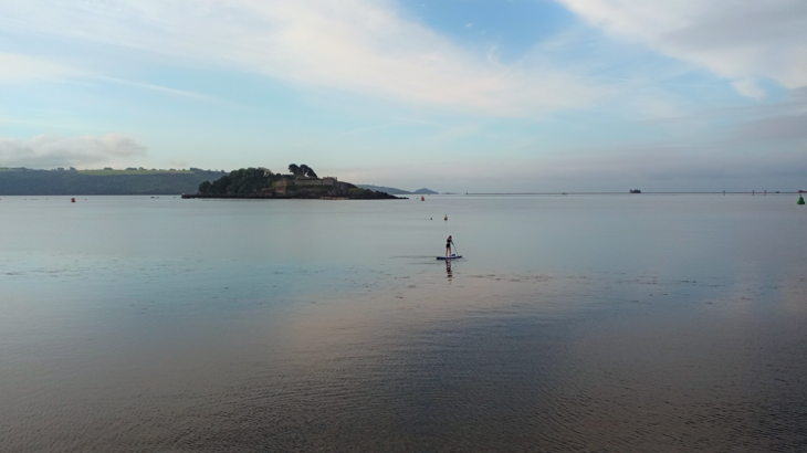 A landscape view of a paddleboarder, paddling across Plymouth Sound in the summer. 