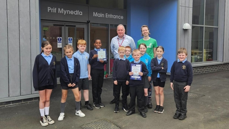 Pupils and staff from Ysgol yr Hafod stand looking at the camera with their Active Travel School Award outside the school entrance.