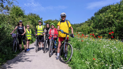 A group of volunteers on their bikes stand next to their flowering patch of wildflowers on a sunny day.