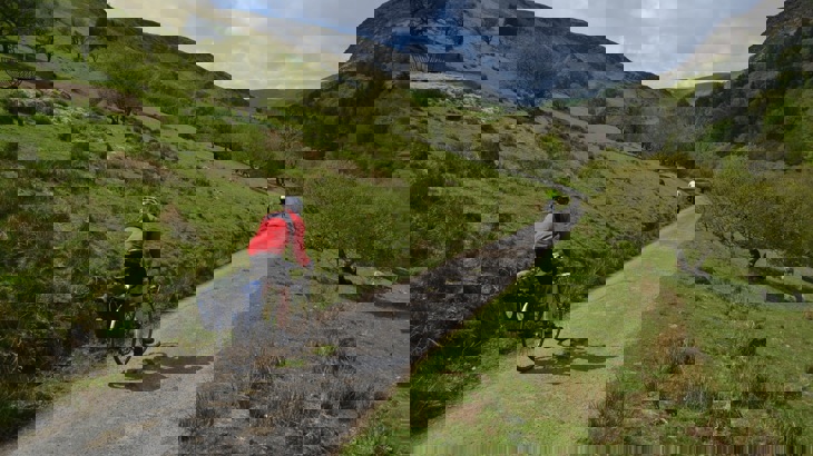 Two road cyclists with panniers, one in red jacket the other in bright green, on gravel track through Welsh mountains