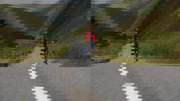 Person riding road bike with panniers wearing red helmet and jersey on road through hills