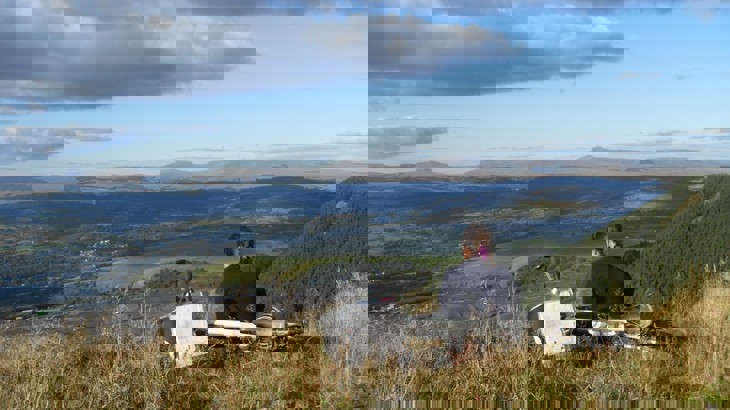 Someone sitting on grassy hillside with bike behind them, looking out on Welsh valley with quarry below