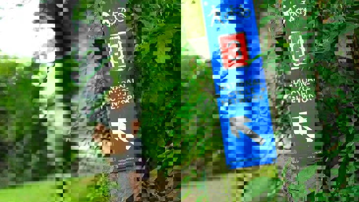 Blue and red sign for National Cycle Network Route 3 with cyclist in background