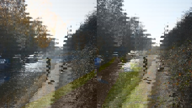 Runner in shorts on canal towpath with narrowboats moored on the opposite bank 