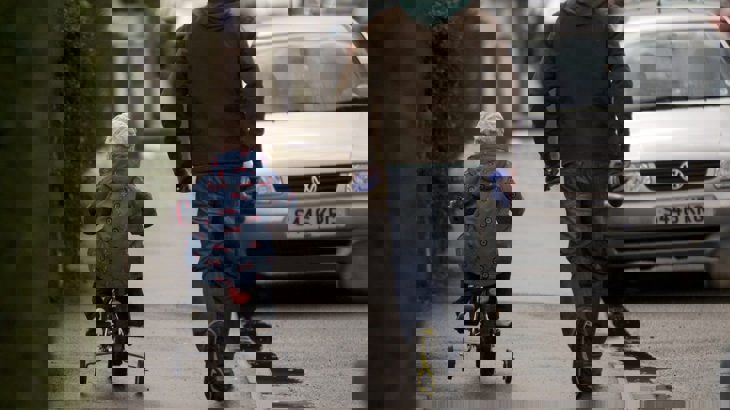 A Man Walking On Pavement While Child Cycles