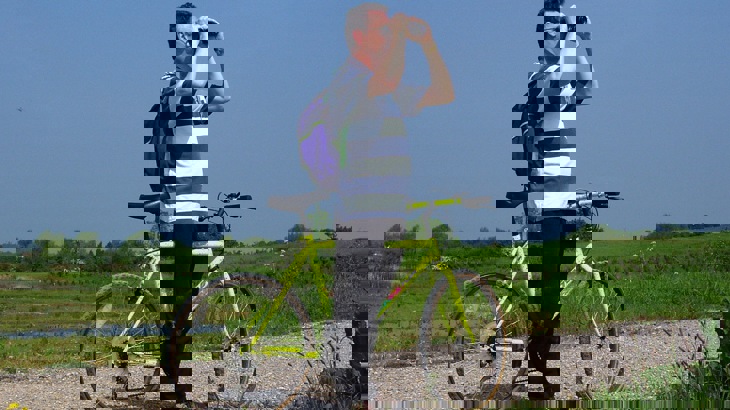 Man with rucksack and bike looking through binoculars in wetland area