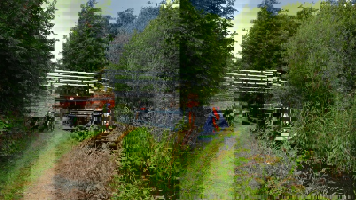Man standing with bike on canal towpath with narrow boat passing under bridge