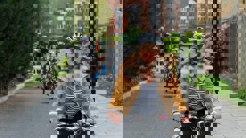 A woman rides a bike on a traffic-free path with an adapted bicycle following in the background 