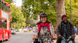 man and woman cycling with red bus in background