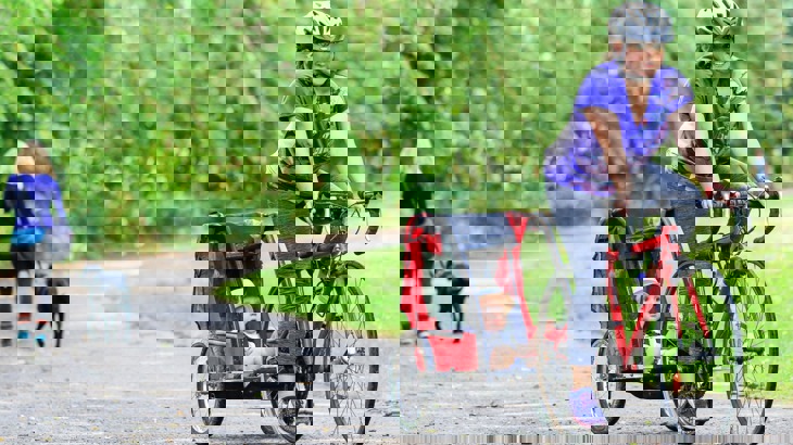 Woman cycling on cycle path pulling small child in trailer