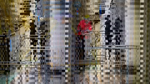 Person on foot with umbrella trying to squeeze past someone on a bicycle through a restrictive barrier on the route