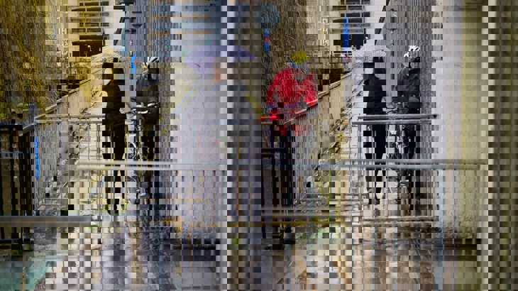 Person on foot with umbrella trying to squeeze past someone on a bicycle through a restrictive barrier on the route