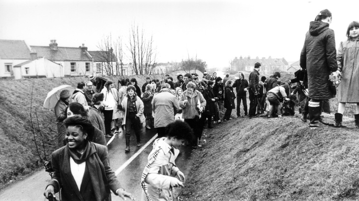Black and white photo of people gathering on a section of cycle path, with grassy banks to the side