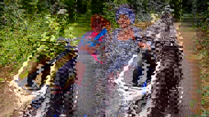 Two women cycling along a traffic-free path using a side-by-side tandem tricycle