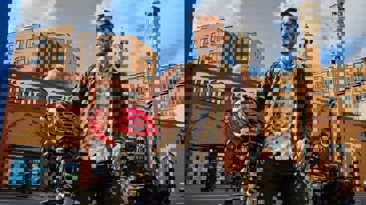 Shaheb stands outside his Mosque with his bicycle and holding his helmet