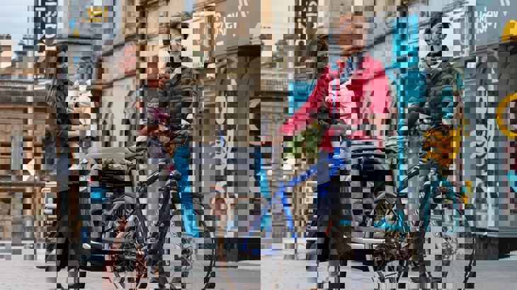 Mum holding baby laughing with friend next to a bicycle with back trailer