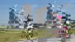 Young girl and woman riding cycles on path near giant horse head sculptures