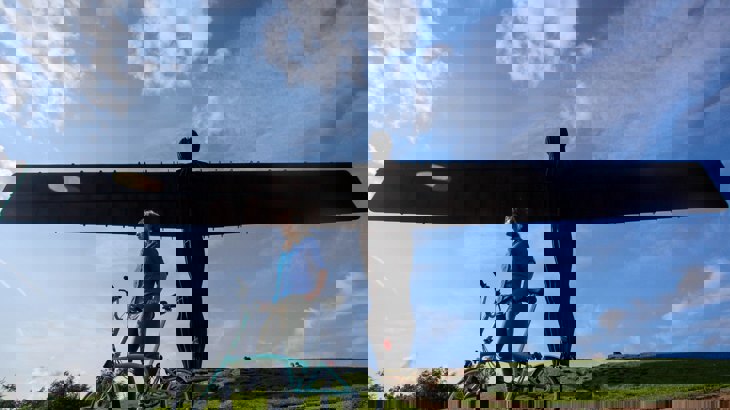 Woman with fold up bike standing in front of large angel sculpture