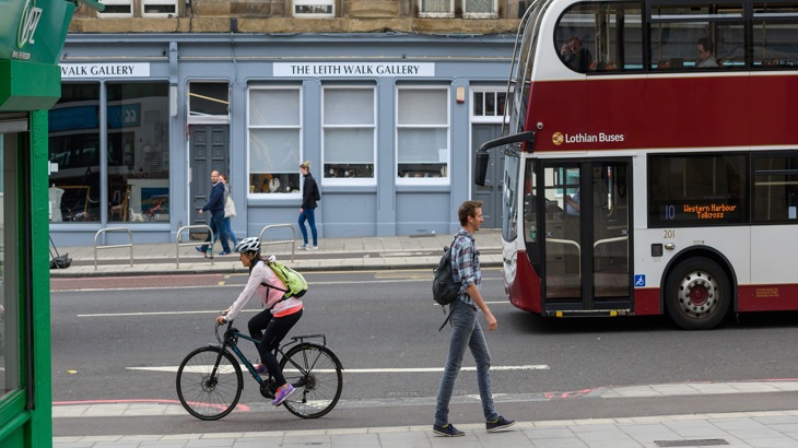 Man walking and woman cycling with bus driving past in background