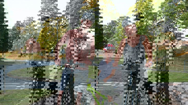 Mum and dad with daughter in a park, wearing helmets and standing with their bikes smiling
