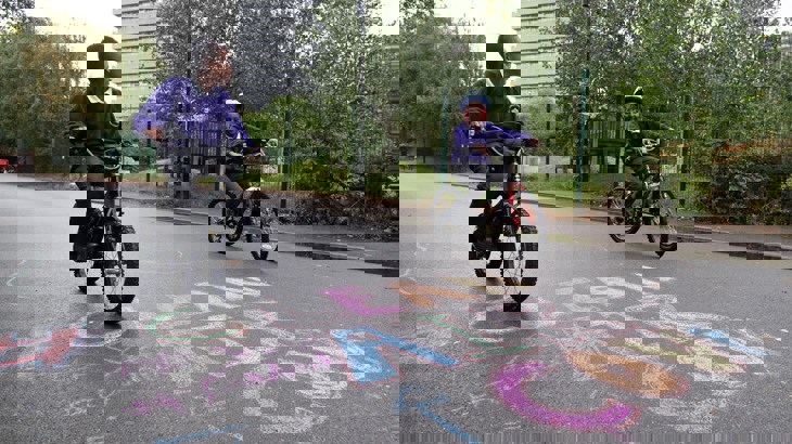 Two school boys cycling in playground with "Clean Air" written in chalk on the ground