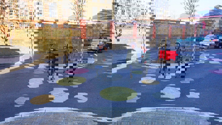 Children walking and cycling across a newly pedestrianised street with colourful drawings on ground outside school