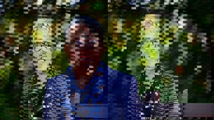 Head shot of Christine Boston, Walk Wheel Cycle Trust in Wales director, wearing glasses, a striped purple top and a navy scarf, smiling with greenery in the background.