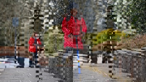 A young girl in school uniform, a winter coat and a helmet rides her scooter. 