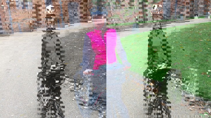 Caroline wearing a black and pink waterproof jacket, black trousers and her cycle helmet, standing with her bicycle.