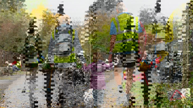Mum and dad holding hands with their small daughter, wearing Walk Wheel Cycle Trust volunteer high-vis jackets and walking away from camera down a traffic-free route.