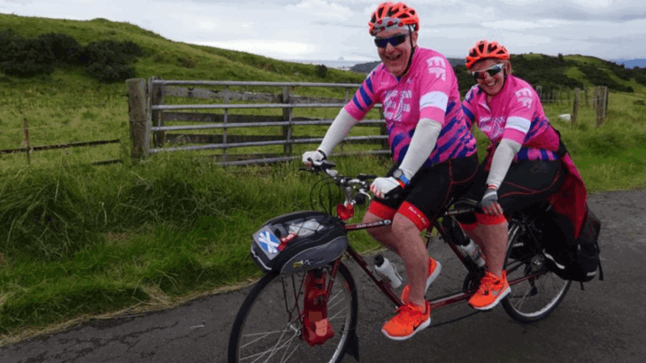 Colin and Diane riding on a tandem bike together, wearing bright neon bike tops and helmets, smiling