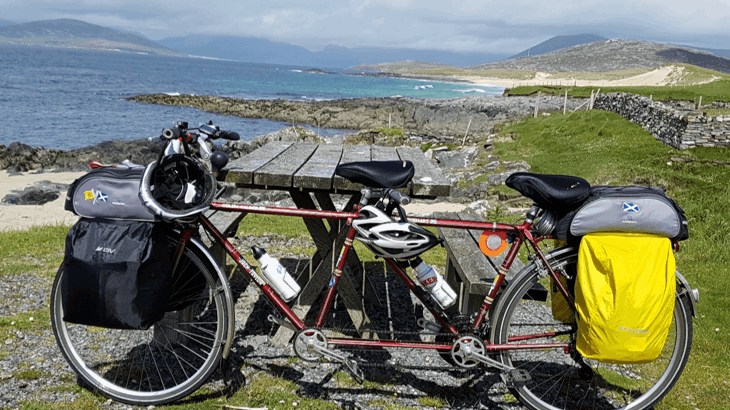 A tandem bike is leaning against a picnic bench, with a Hebridean beach in the background.