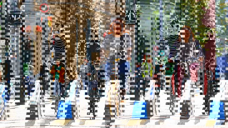 Two Women Cycling Through Barriers On Street In Manchester
