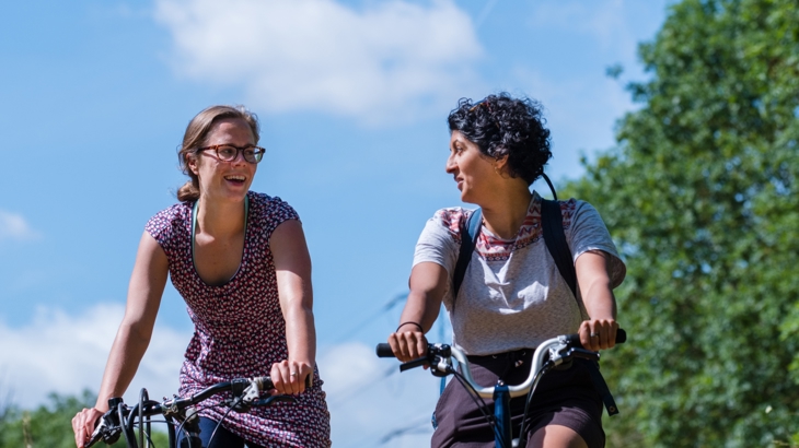 two females cycling on sunny day with trees in background