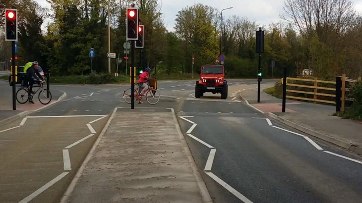 A road crossing with traffic lights and cyclists going over the road.