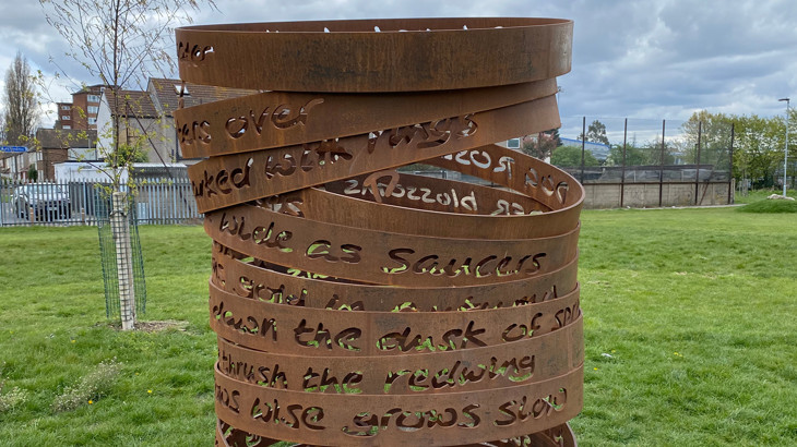 Close up photo of a metal art installation along the Ripple Greenway in London. The installation is a spiral artwork with poems engraved all around it.