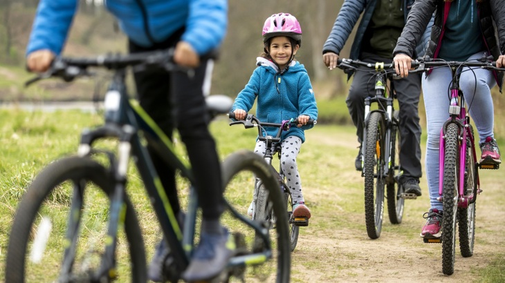 Young girl cycling with pink helmet. Someone riding a bike in foreground and bikes in background. 
