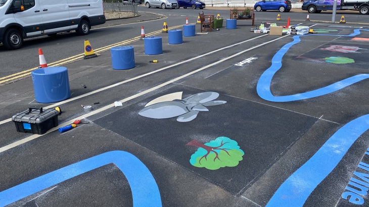 Artwork on the ground including a tree, barriers and benches with a co-op shop in the background.